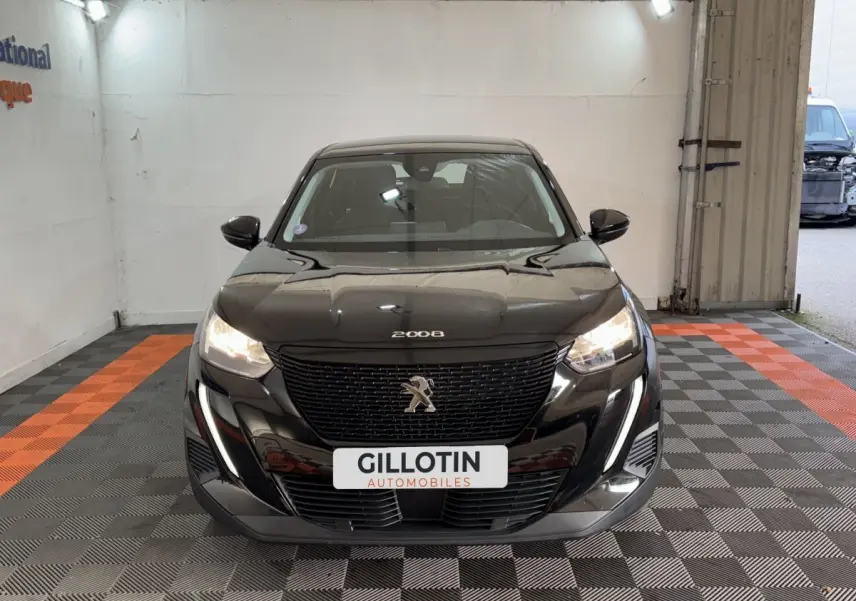 Vue frontale d'une Peugeot 2008 noire 2022 avec phares allumés et calandre imposante dans un garage.