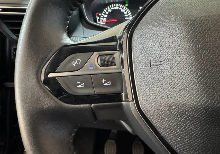 Gros plan sur le volant cuir noir du Peugeot 2008 2022, côté gauche avec commandes audio et tableau de bord partiel.