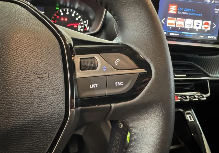 Gros plan sur le volant cuir noir de la Peugeot 2008 2022, avec commandes audio et écran tactile du tableau de bord visible.