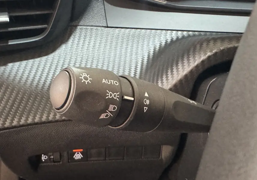 Gros plan sur la commande des phares à gauche du volant dans l’habitacle noir du Peugeot 2008 PureTech 130 S&S ACTIVE PACK.