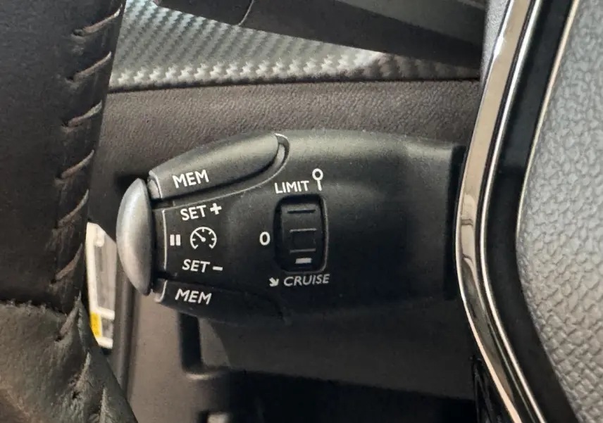 Gros plan sur la commande de régulateur de vitesse noire avec marquages blancs, sur le volant cuir d’un Peugeot 2008 noir.