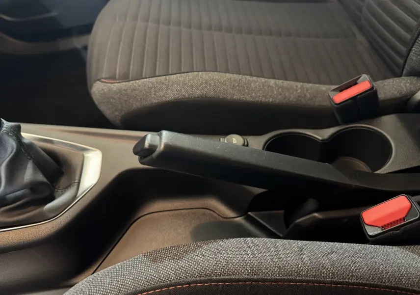 Vue rapprochée de la console centrale intérieure du Peugeot 2008 2022 noire, avec frein à main manuel et sièges tissu gris.