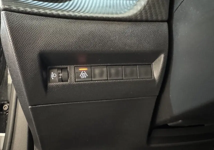 Vue rapprochée du tableau de bord côté conducteur de la Peugeot 2008 noire, avec commandes d'éclairage et d'assistance activée.