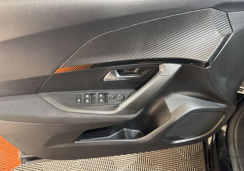 Vue rapprochée de la porte côté conducteur du Peugeot 2008 noir, avec insert décoratif carbone et commandes électriques.