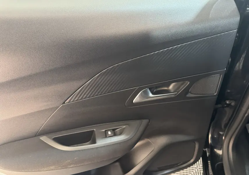 Vue intérieure côté droit de la porte avant noire du Peugeot 2008 avec poignée argentée et habillage effet carbone.