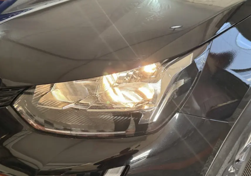 Gros plan sur le phare avant droit allumé d’un Peugeot 2008 noir, soulignant les lignes modernes du capot.