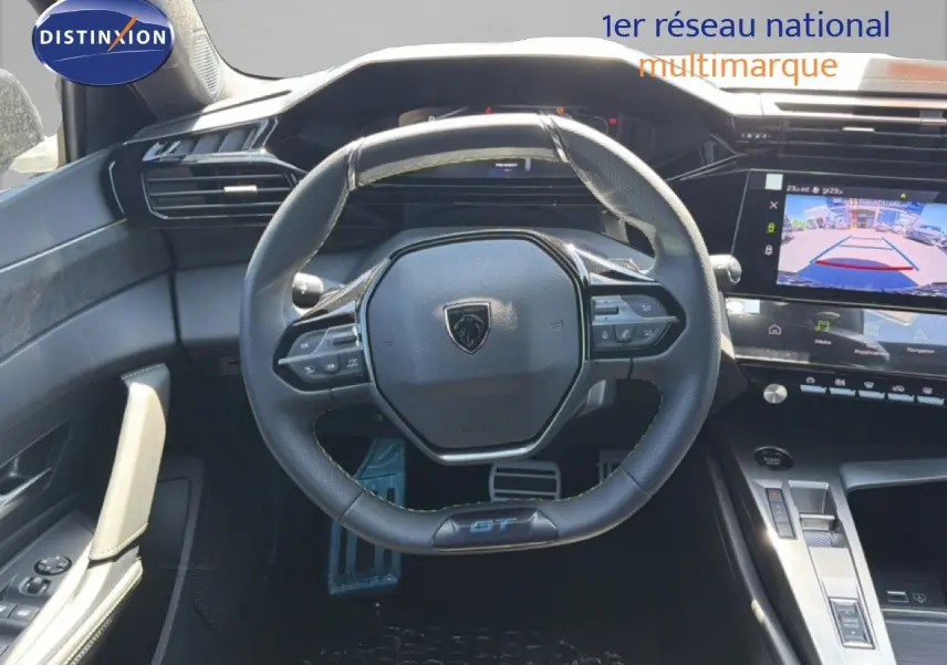 Vue intérieure centrée sur le volant cuir noir de la Peugeot 308 Hybrid 145ch GT avec écran tactile et caméra de recul affichée.