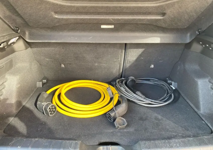 Coffre ouvert d'un Jeep Avenger électrique noir 2023, avec câbles de recharge jaune et noir rangés à l'intérieur.