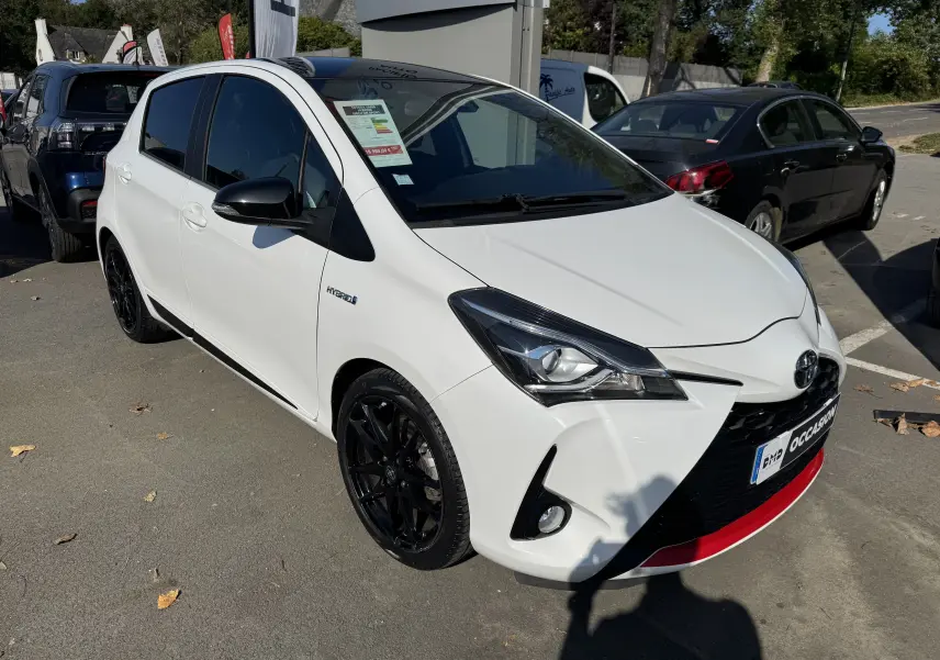 Toyota Yaris Hybride 100CH GR SPORT blanc vue 3/4 avant droit avec jantes noires et détails rouges sur le pare-chocs.