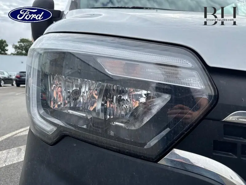 Gros plan sur le phare avant droit d'un Renault Master blanc minéral, soulignant les détails du bloc optique et la calandre noire.