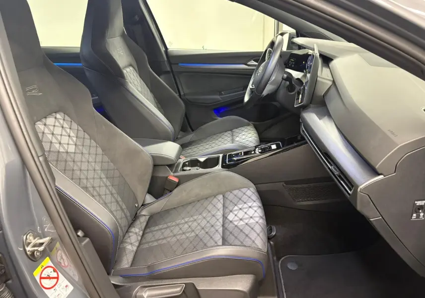 Vue intérieure côté conducteur de la Volkswagen Golf 1.5 eTSI R-Line Edition 2025 avec sièges gris à surpiqûres bleues et tableau de bord moderne.