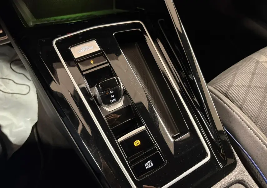 Gros plan sur la console centrale noire brillante de la Volkswagen Golf 1.5 eTSI 2025 avec levier de vitesses automatique et bouton start/stop.