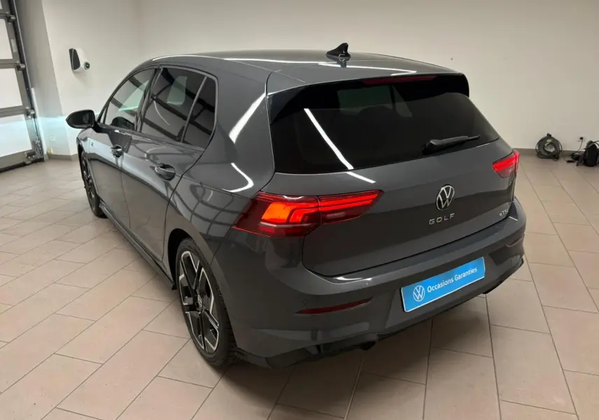 Vue 3/4 arrière d'une Volkswagen Golf 1.5 eTSI gris dauphin avec feux arrière allumés en intérieur showroom.