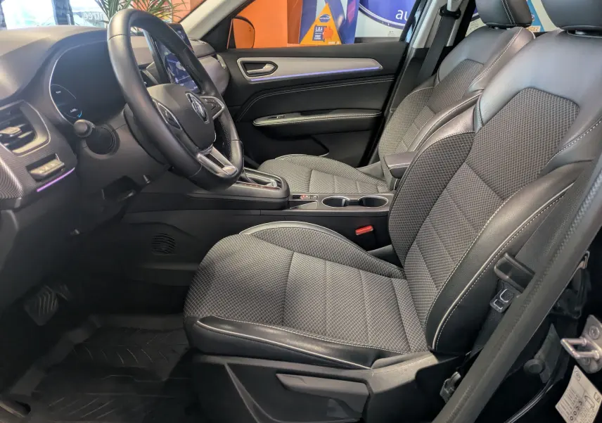 Vue intérieure côté conducteur du Renault Arkana 2023 noir, mettant en valeur les sièges en tissu et cuir avec console centrale et volant multifonction.