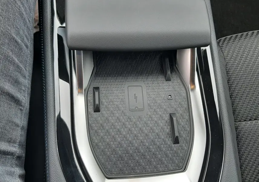Vue plongeante sur la console centrale noire du Renault Austral hybride, mettant en valeur le chargeur à induction et l'accoudoir gris.