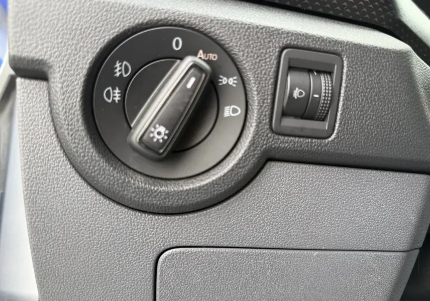 Gros plan sur le sélecteur de phares noir et la molette de réglage d’intensité lumineuse dans l’habitacle gris du Volkswagen T-Cross 2019.