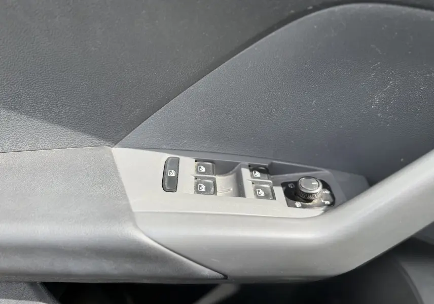 Gros plan sur la commande des vitres électriques et réglage des rétroviseurs côté conducteur d’un Volkswagen T-Cross gris 2019.