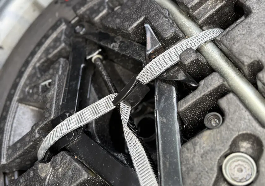 Gros plan sur le coffre d’un Volkswagen T-Cross 2019 gris, montrant la roue de secours et les outils attachés par une sangle.