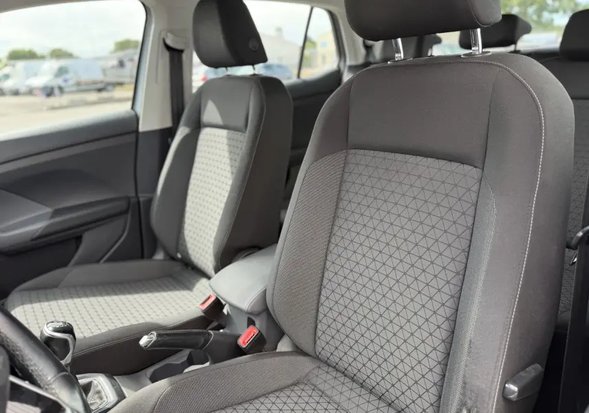 Vue intérieure côté gauche du Volkswagen T-Cross gris 2019, montrant les sièges avant en tissu et la boîte manuelle.