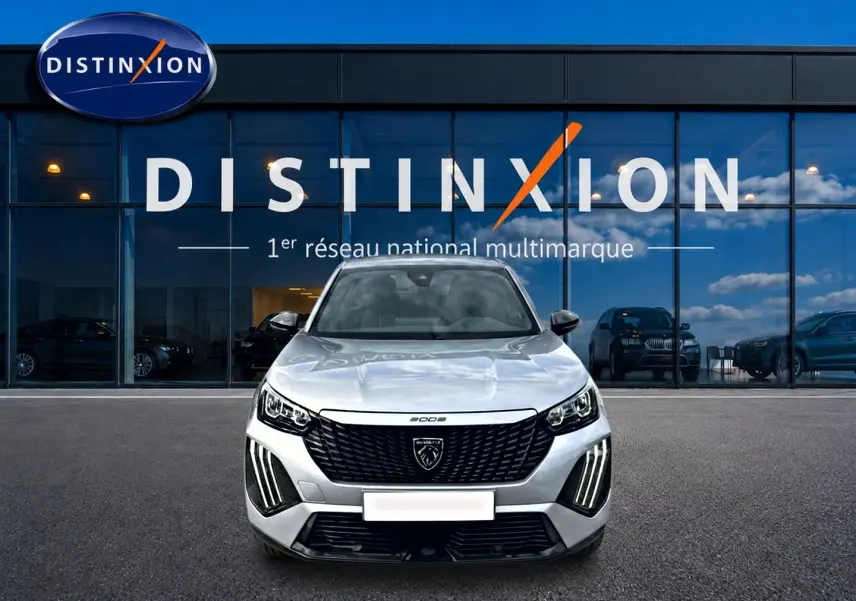 Vue avant d'un Peugeot 2008 gris 2025 avec calandre noire et feux LED distinctifs, devant une vitrine Distinxion.