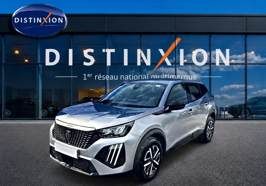 Peugeot 2008 gris en 3/4 avant droit, avec calandre noire et phares LED distinctifs, devant une vitrine Distinxion.