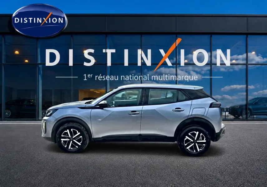 Profil côté gauche du Peugeot 2008 gris 2025 avec jantes noires et toit contrasté blanc devant une vitrine Distinxion.