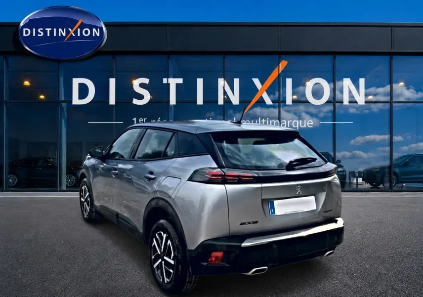 Peugeot 2008 gris en 3/4 arrière droit, avec feux arrière LED et becquet noir, devant une vitrine Distinxion.
