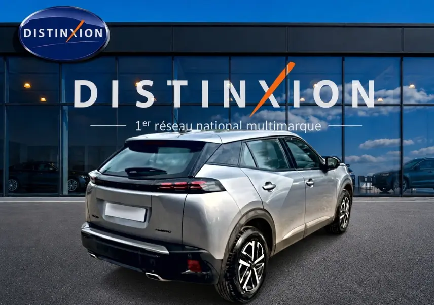 Peugeot 2008 gris en 3/4 arrière droit, avec becquet et feux arrière LED, devant une vitrine Distinxion.