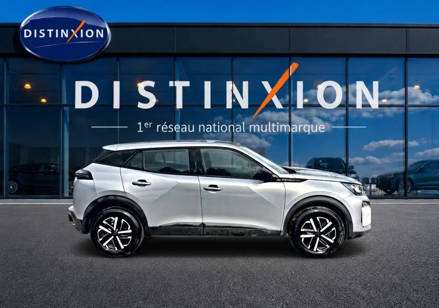 Profil droit du Peugeot 2008 gris 2025 avec jantes noires et toit noir devant une vitrine Distinxion.