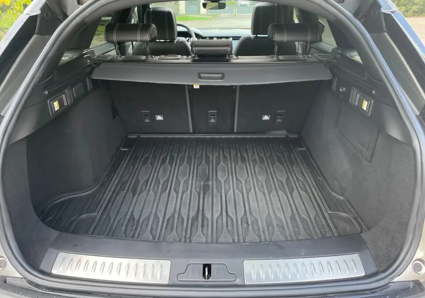 Coffre ouvert d’un Range Rover Velar gris 2019, montrant un tapis de coffre en caoutchouc et banquette arrière en cuir noir.