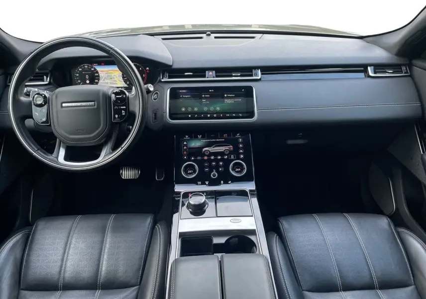 Vue intérieure du tableau de bord et console centrale du Range Rover Velar gris, avec écran tactile et volant multifonction.