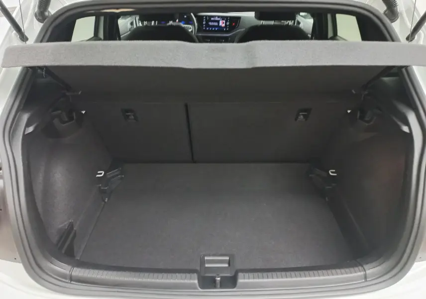 Coffre ouvert d'une Volkswagen Polo blanc pur vue de l'arrière, montrant l'espace de chargement et l'intérieur sombre.
