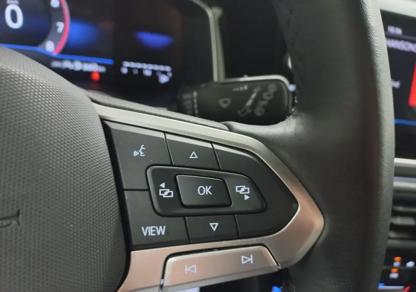 Gros plan sur les commandes multifonctions du volant noir de la Volkswagen Polo 2025, avec écran numérique en arrière-plan.