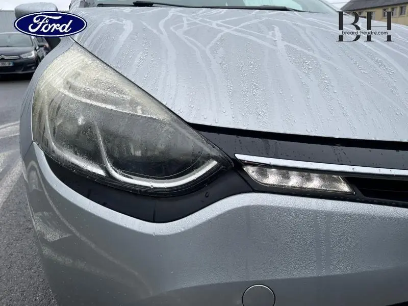 Gros plan sur le phare avant gauche gris platine d'une Renault Clio 2016 avec gouttes d'eau sur la carrosserie.