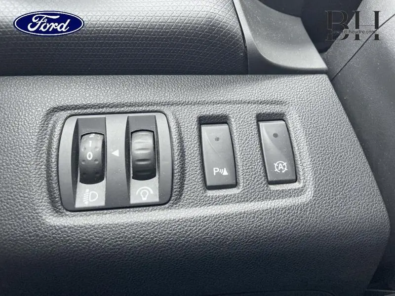 Détail des commandes d’éclairage et d’aide au stationnement sur tableau de bord noir d’une Renault Clio gris platine.