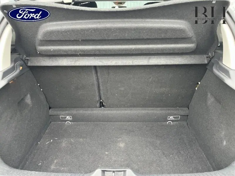 Coffre ouvert vu de l'arrière d'une Renault Clio gris platine, espace de chargement vide et tapis noir.