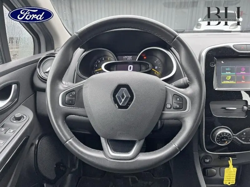 Vue intérieure centrée sur le volant cuir noir d'une Renault Clio gris platine, avec tableau de bord et écran tactile visibles.