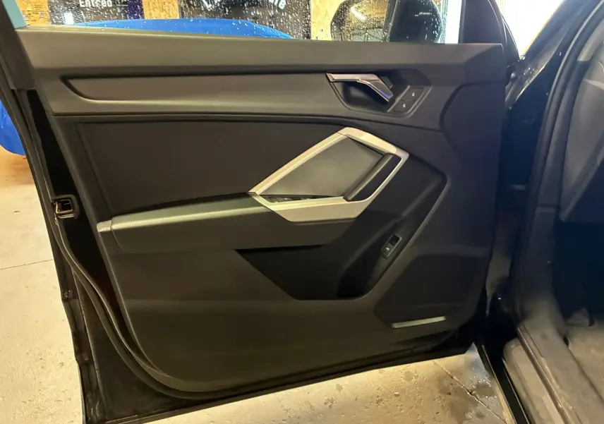 Vue intérieure de la porte avant gauche noire de l'Audi Q3 Sportback 2022 avec détails des commandes et poignée argentée.