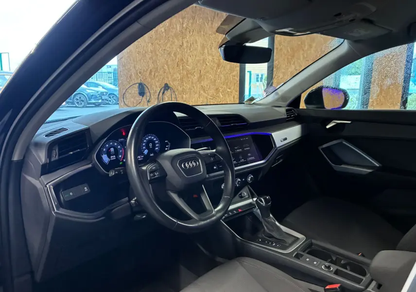 Vue intérieure côté conducteur de l'Audi Q3 Sportback noire 2022, volant cuir multifonctions et écran tactile lumineux.