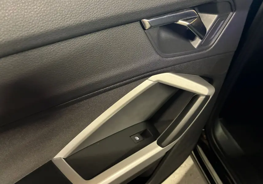 Détail de la porte intérieure côté gauche de l'Audi Q3 Sportback noire avec poignée argentée et commande de vitre électrique.