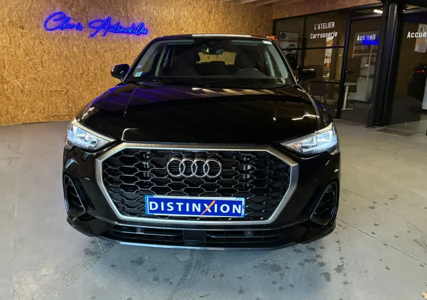 Vue avant d'un Audi Q3 Sportback noir 2022 avec calandre hexagonale et phares LED allumés en intérieur showroom.