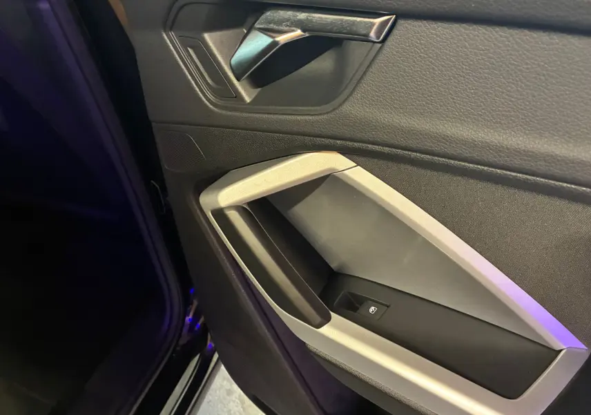 Gros plan sur la poignée intérieure et la commande de vitre côté gauche d’un Audi Q3 Sportback noir 2022.