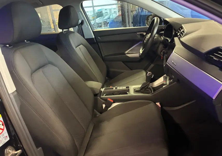 Vue intérieure côté conducteur de l'Audi Q3 Sportback 2022 noire, sièges en tissu noir et tableau de bord moderne.