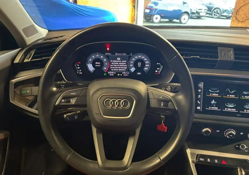Vue intérieure centrée sur le volant cuir multifonctions d'un Audi Q3 Sportback 2022 avec tableau de bord numérique et écran tactile.