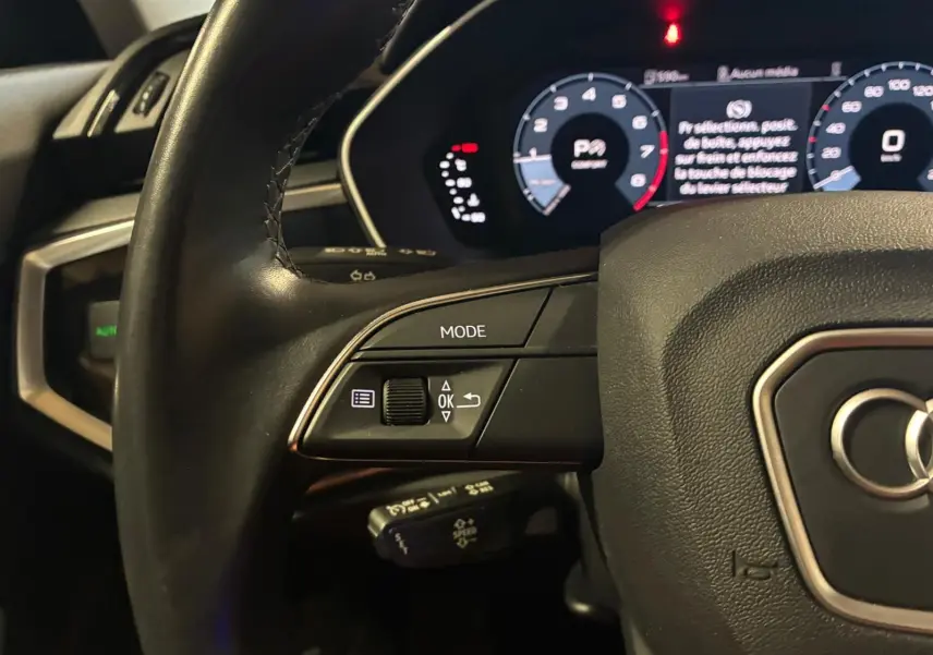 Gros plan sur le volant cuir multifonctions noir de l'Audi Q3 Sportback 2022 avec tableau de bord numérique éclairé.