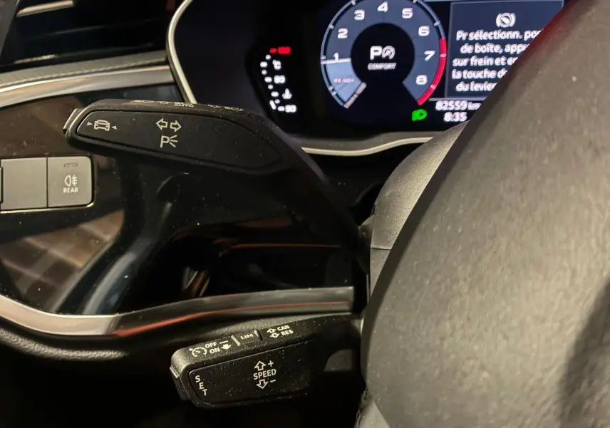 Gros plan sur les commandes au volant d’un Audi Q3 Sportback noir, avec tableau de bord numérique allumé.