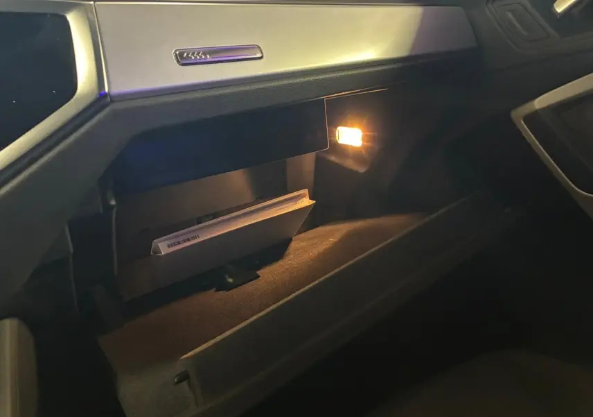 Gros plan sur la boîte à gants ouverte de l’Audi Q3 Sportback 2022 avec lumière intérieure allumée et manuel visible.