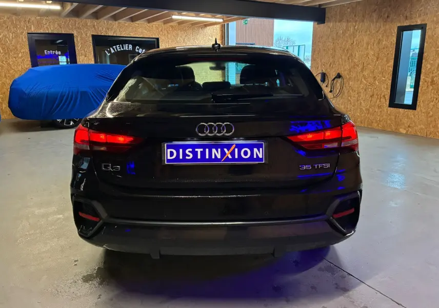 Vue arrière d'un Audi Q3 Sportback noir 2022 avec feux allumés dans un garage intérieur.
