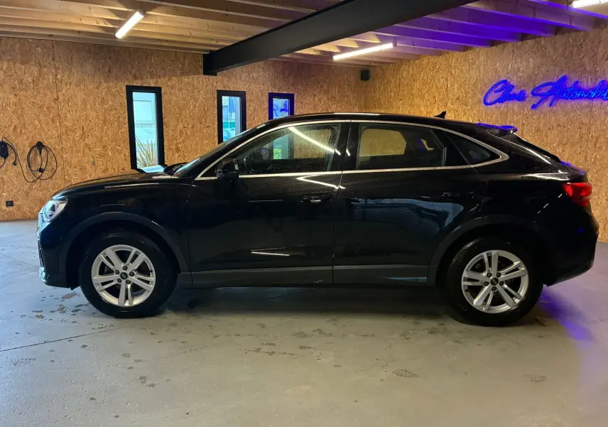 Audi Q3 Sportback noir vue de profil côté gauche, jantes alliage, stationné en intérieur avec éclairage néon bleu.