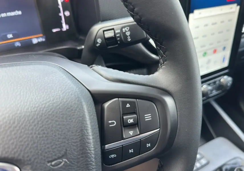Gros plan sur le volant cuir multifonctions du Ford Ranger gris iconic, avec écran tactile et commandes au volant visibles.
